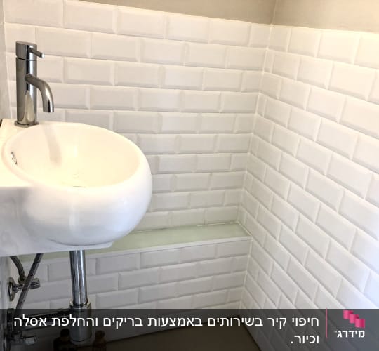 כיור לבן עם ברז מתכת על קיר אריחים לבנים